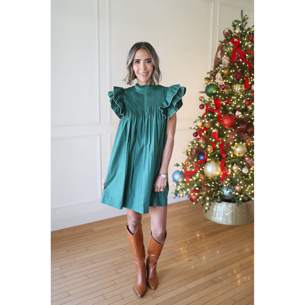 Woman in a green dress standing next to a decorated Christmas tree.