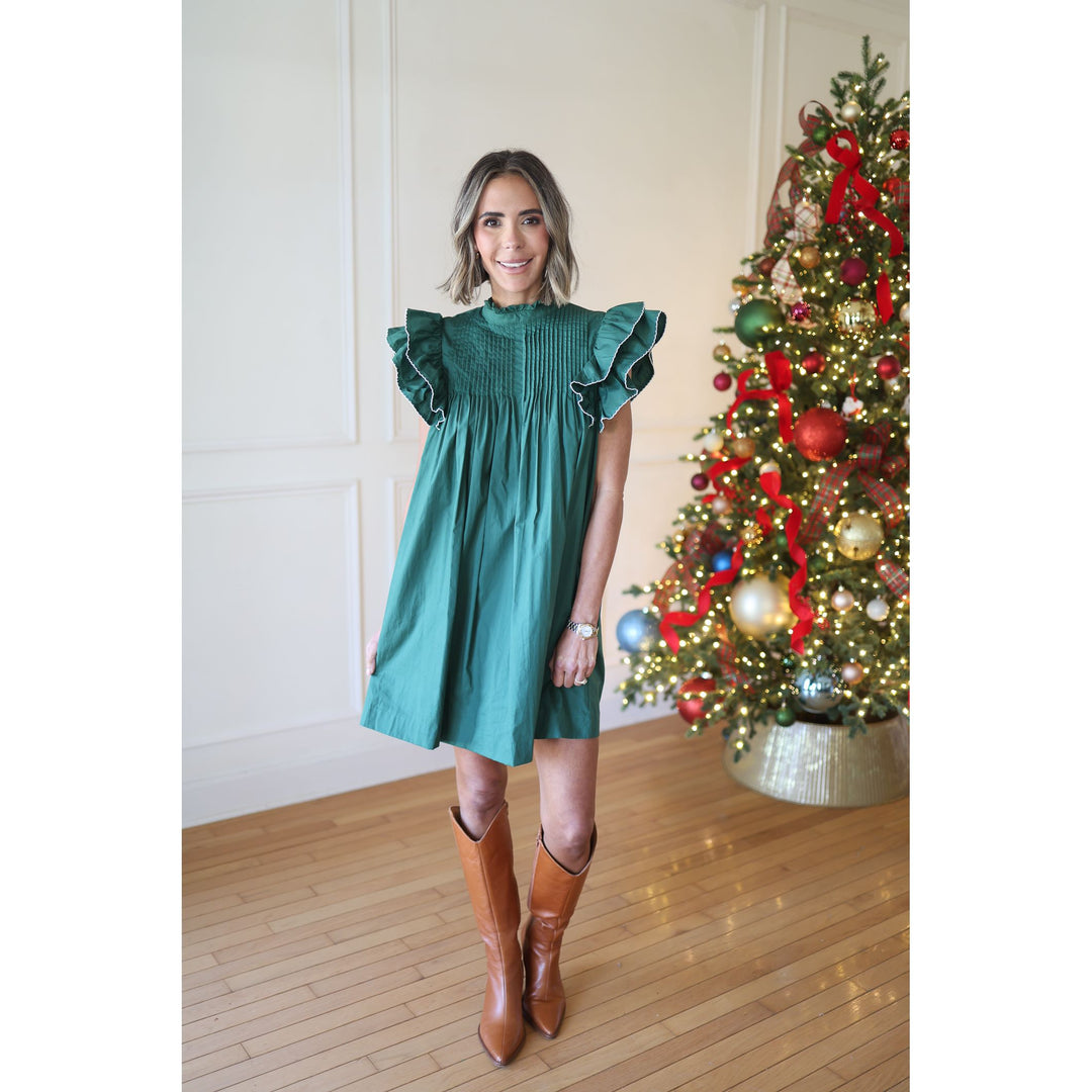 Woman in a green dress standing next to a decorated Christmas tree.