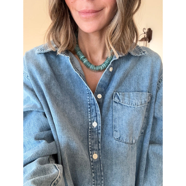 Person wearing a light blue denim shirt with a emerald necklace