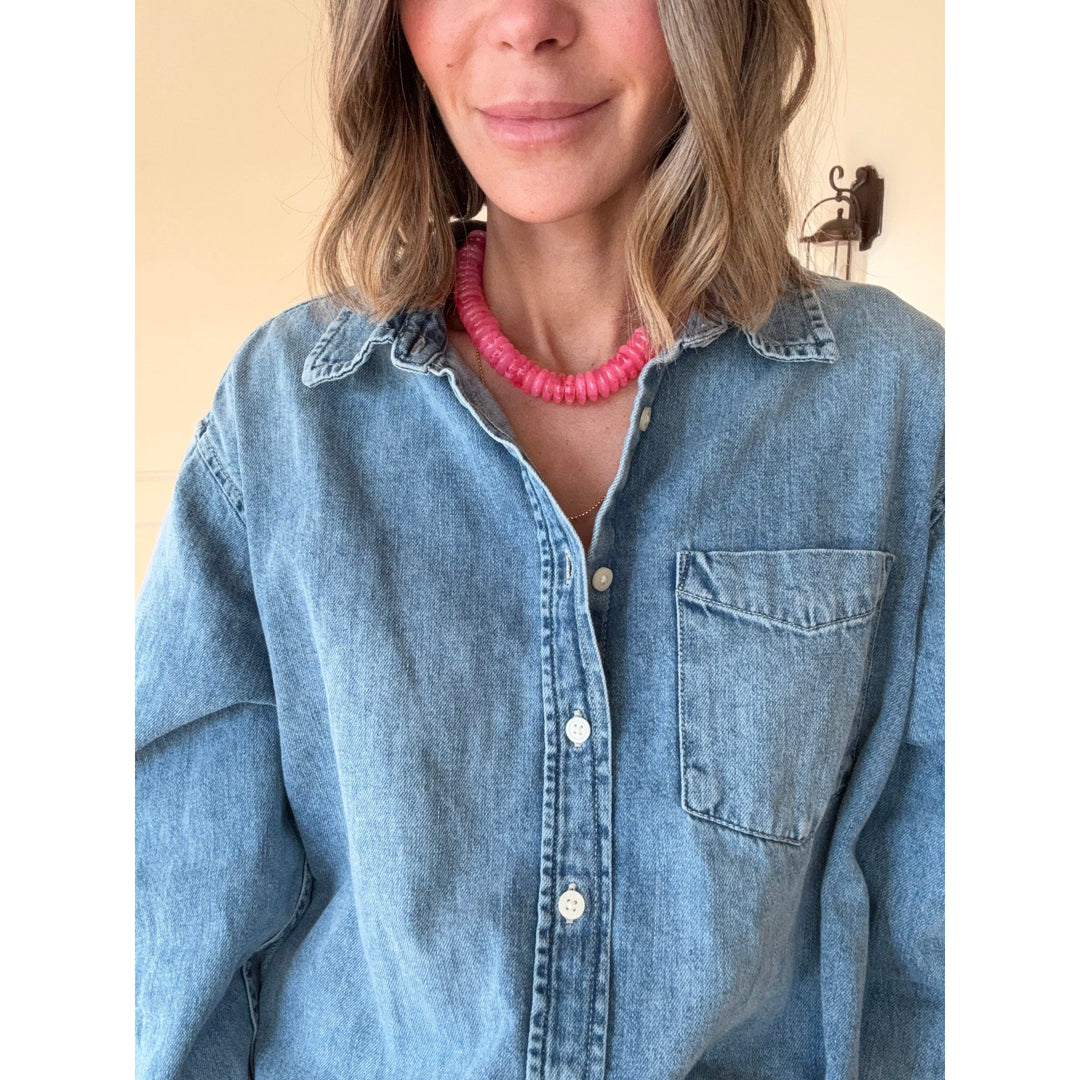Person wearing a blue denim shirt with a pink necklace