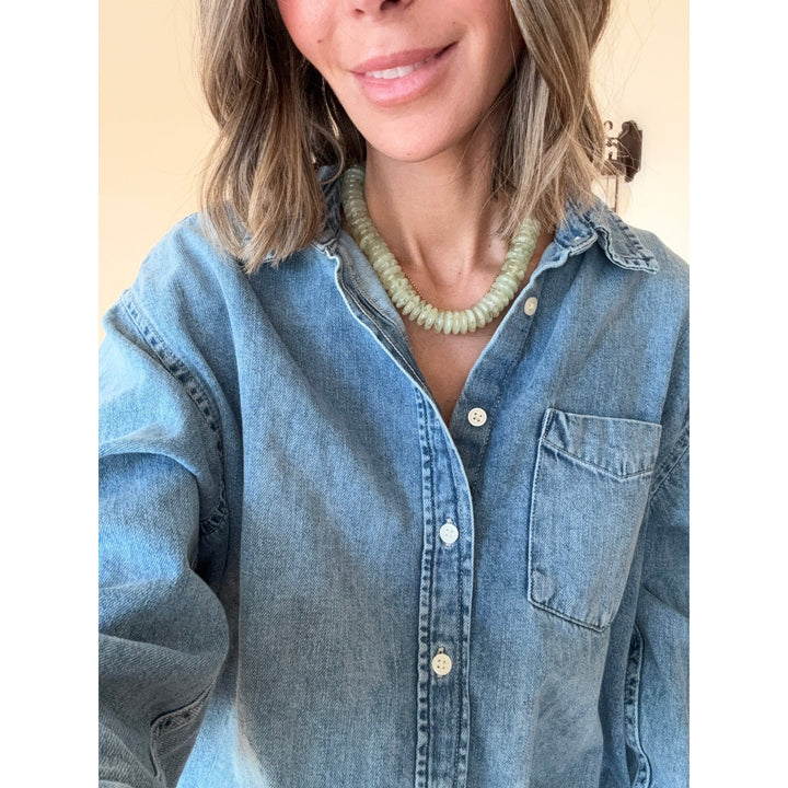 Person wearing a blue denim shirt with a sage green necklace