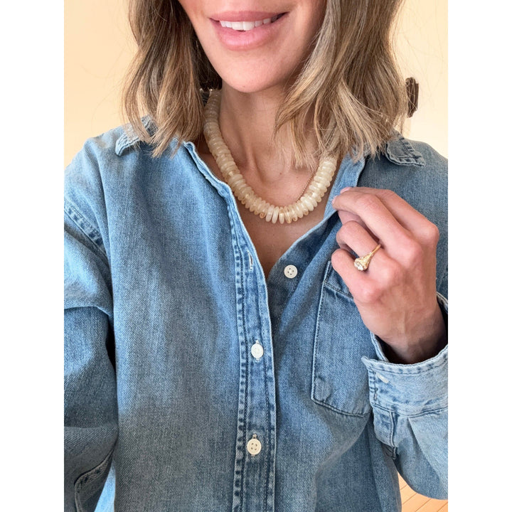 Person wearing a blue denim shirt with a pearl necklace  