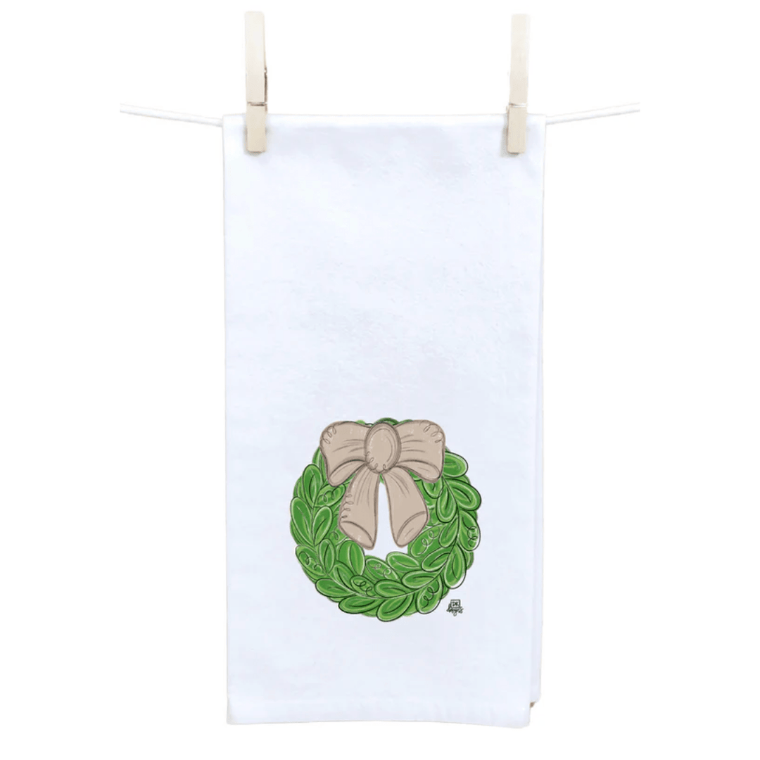 White towel with a green wreath and beige bow design, hanging on a line.