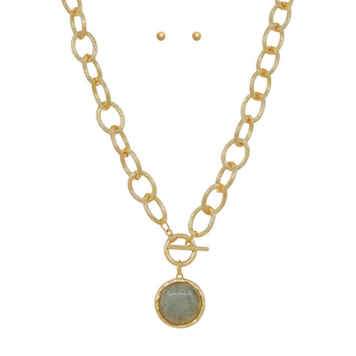 A gold chain necklace with a toggle clasp and a round bezel-set stone pendant, shown with two small matching stud earrings.