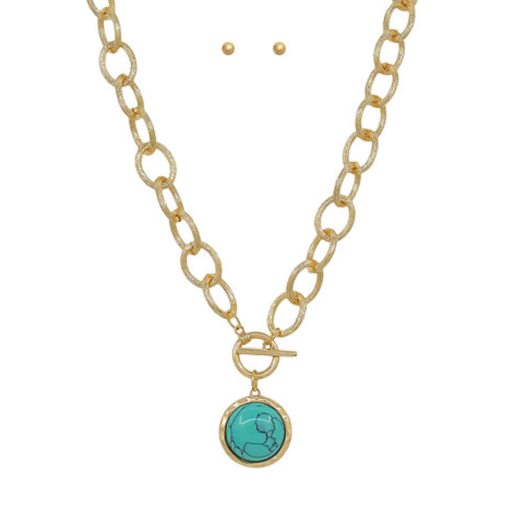 Gold chain necklace with a toggle clasp and a round turquoise pendant shown with two matching gold stud earrings.