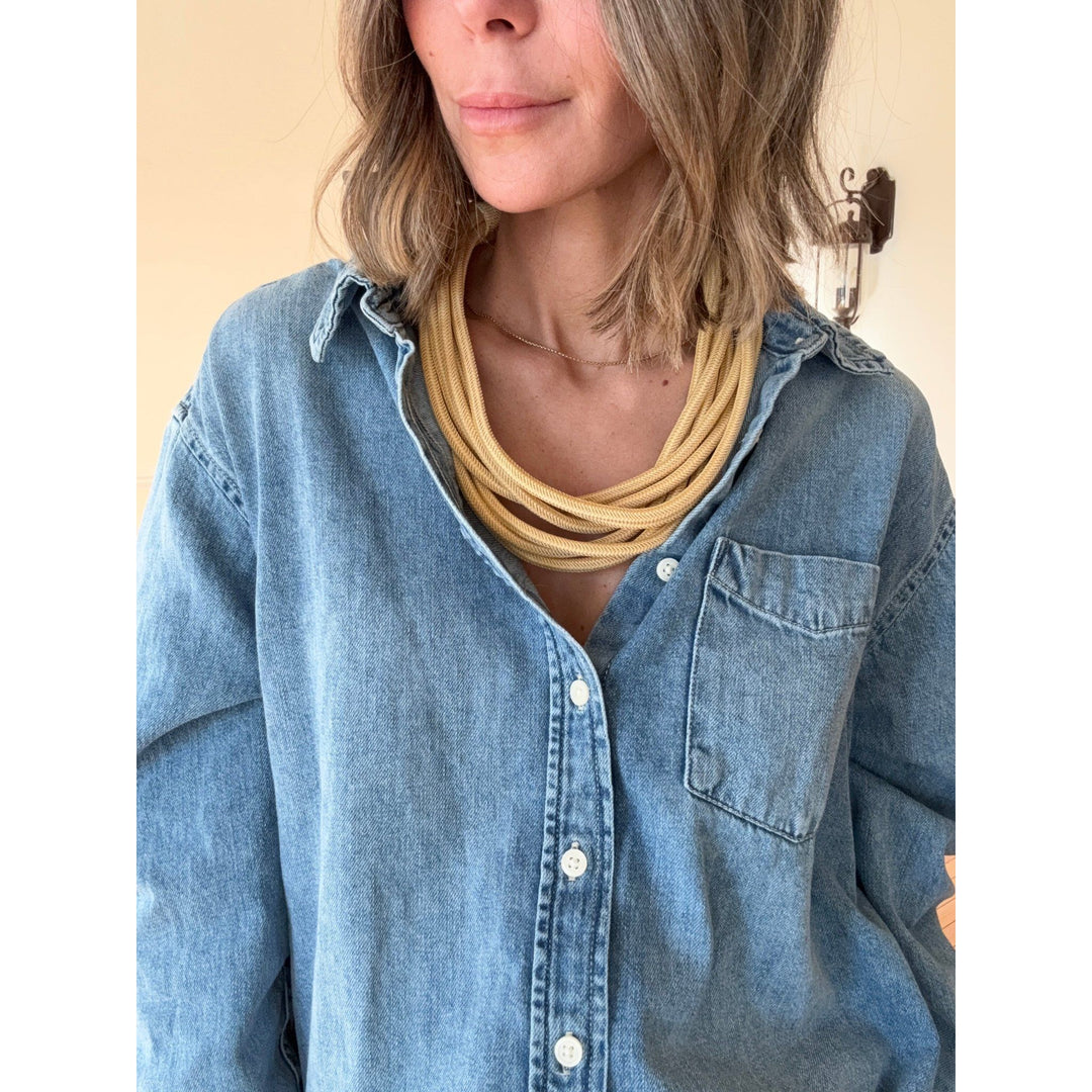 Person wearing a blue denim shirt with a gold rope necklace