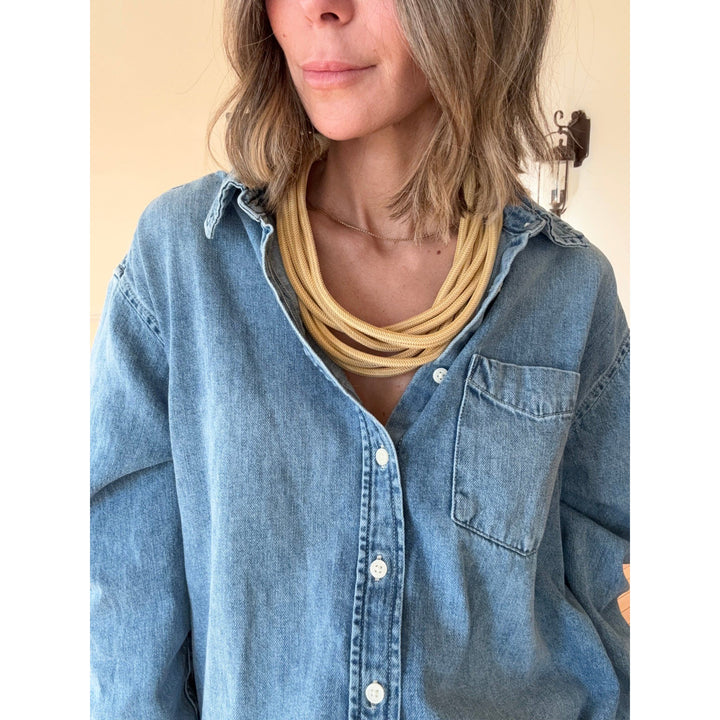 Person wearing a blue denim shirt with a gold rope necklace