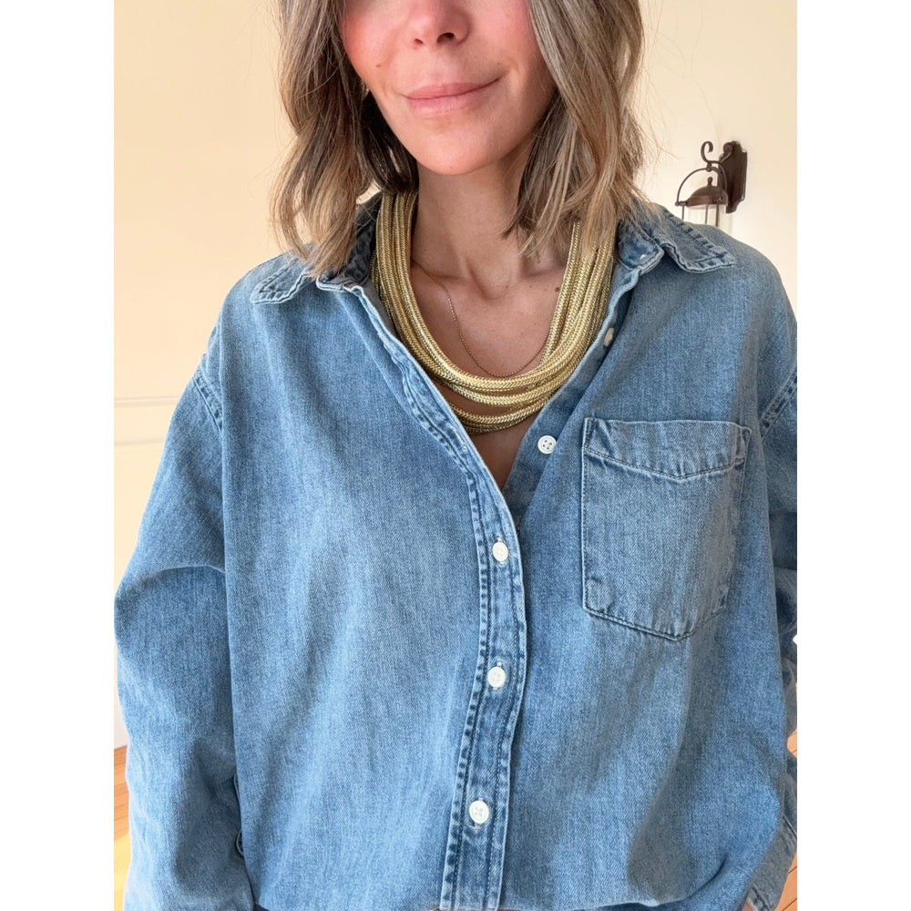 Person wearing a blue denim shirt with a gold necklace