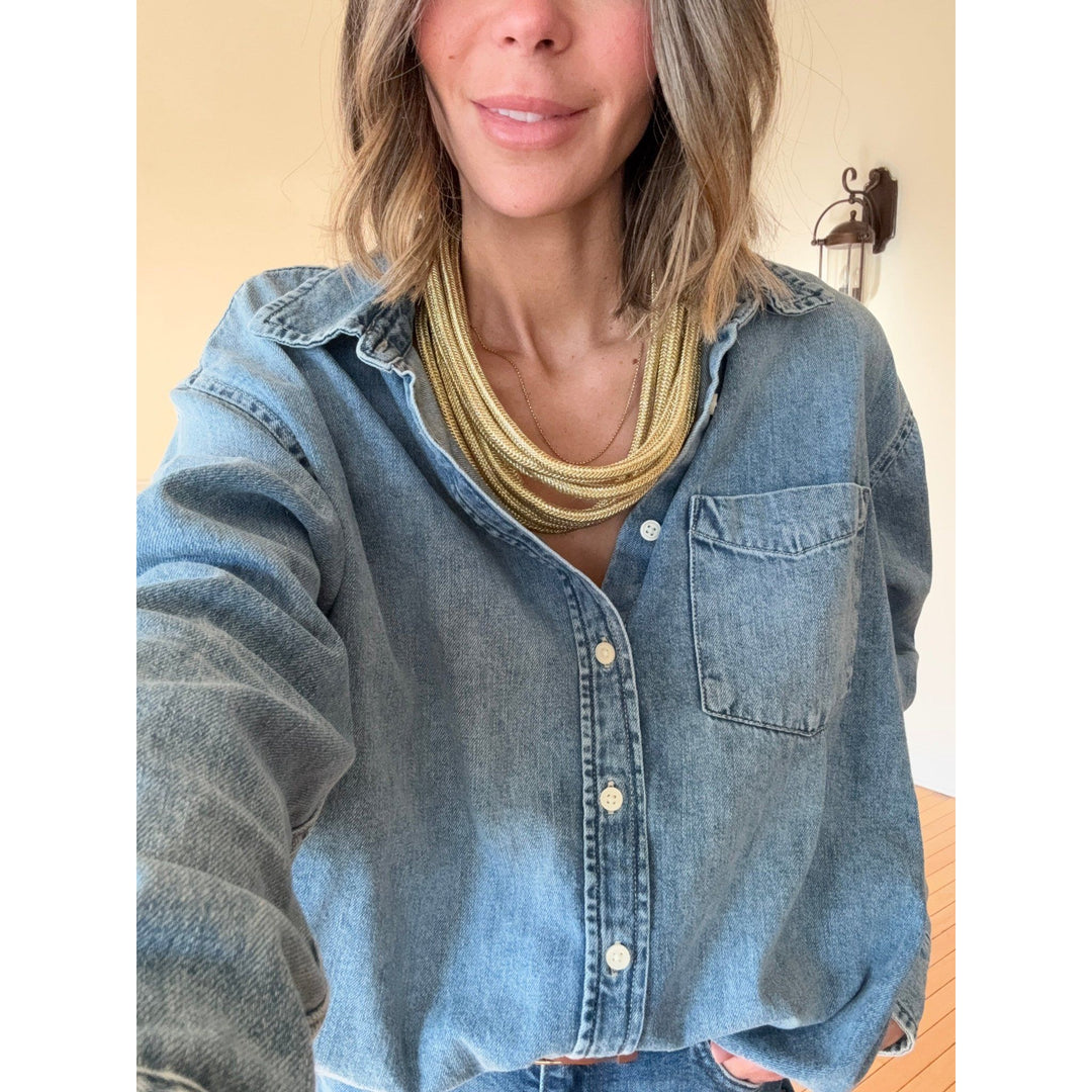 Person wearing a denim shirt with a gold necklace indoors.