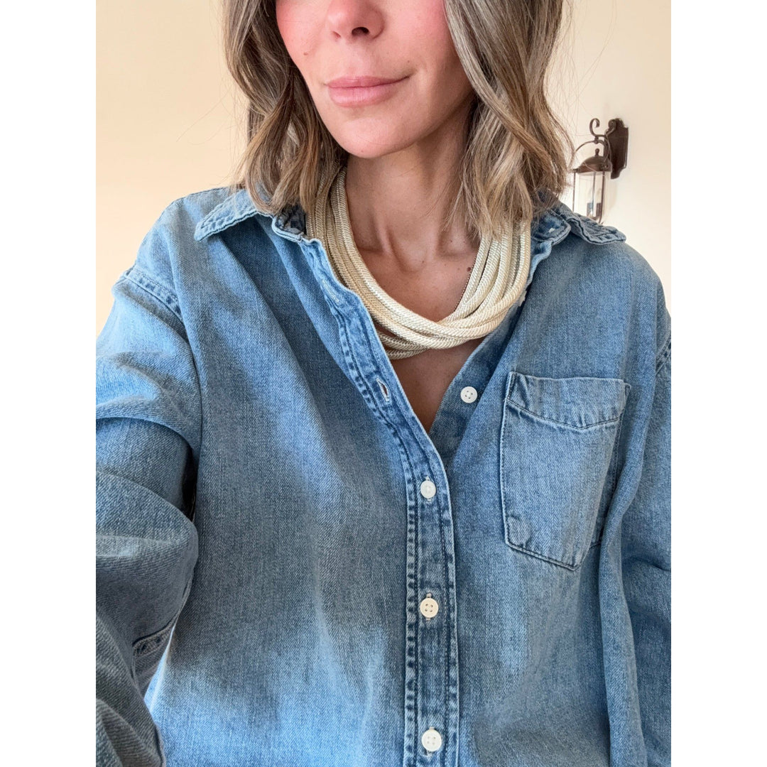 Person wearing a blue denim shirt with a tan necklace