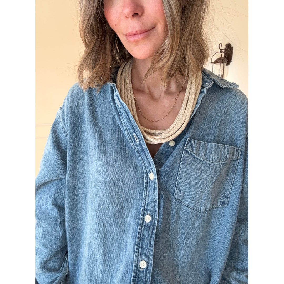 Person wearing a blue denim shirt with a tan necklace