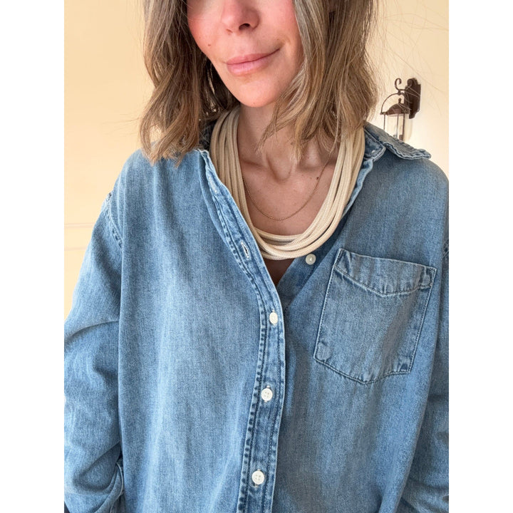 Person wearing a blue denim shirt with a tan necklace