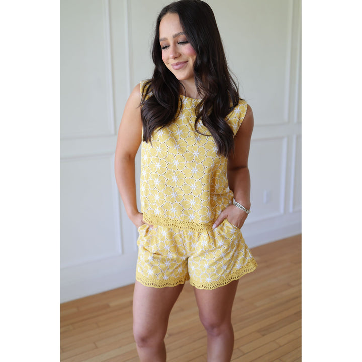 Woman wearing a yellow floral romper in a room with wooden flooring and white walls.