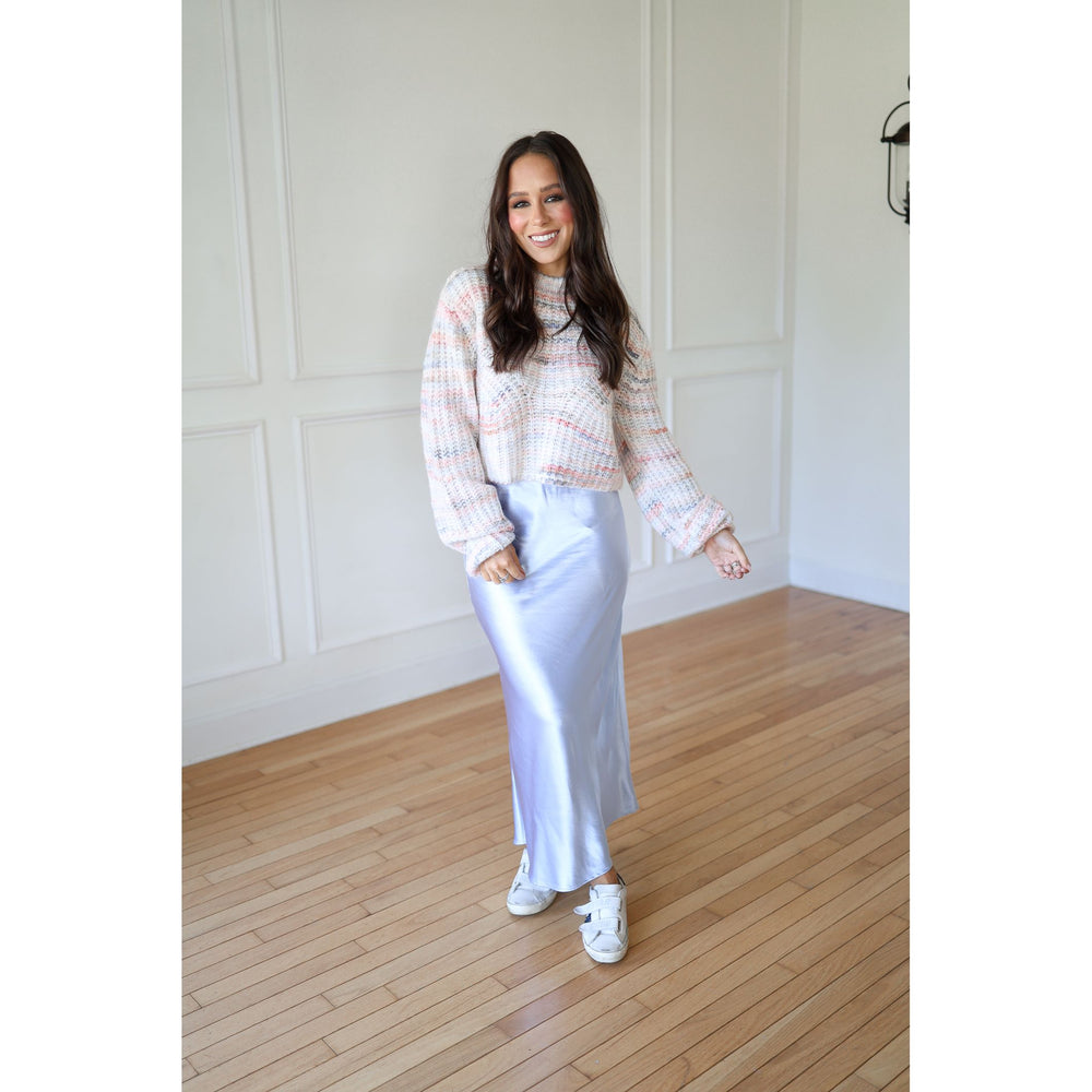Woman in a plaid shirt and silver skirt standing on a wooden floor with a white wall background