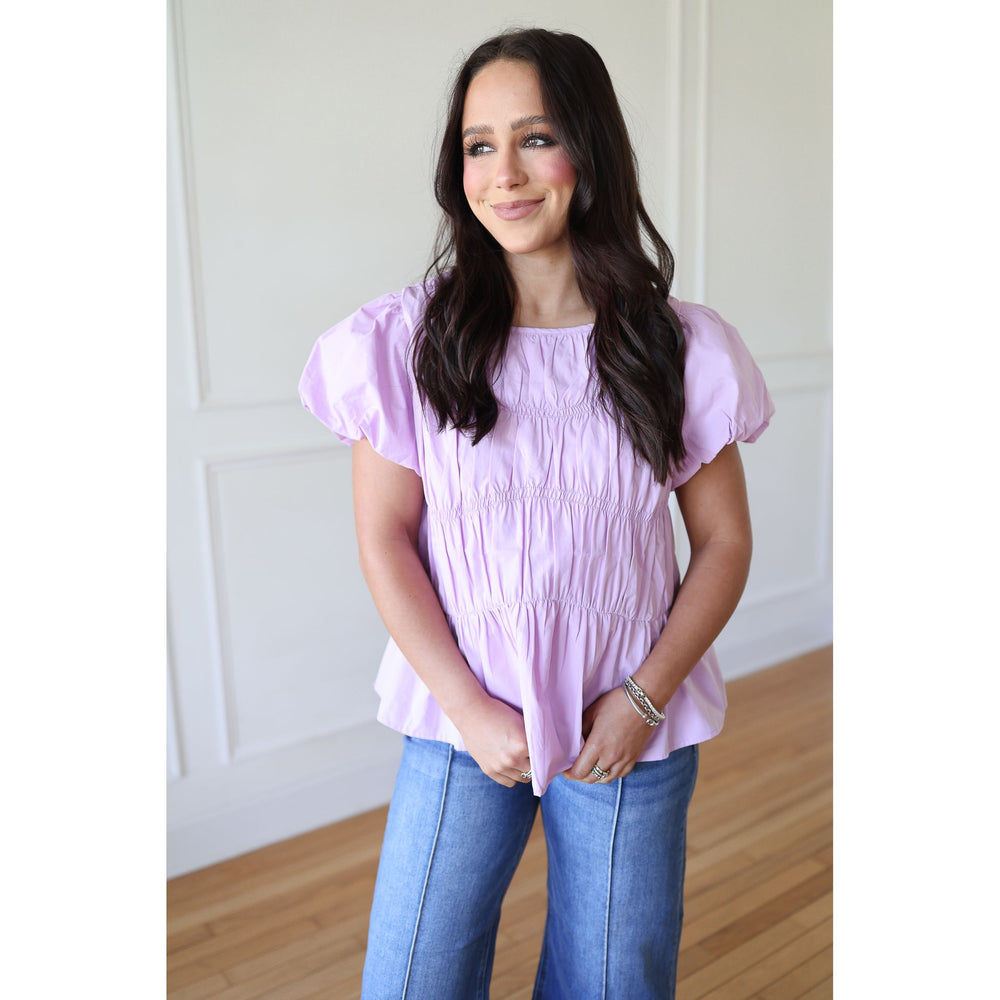 Woman wearing a light purple top and blue jeans indoors.