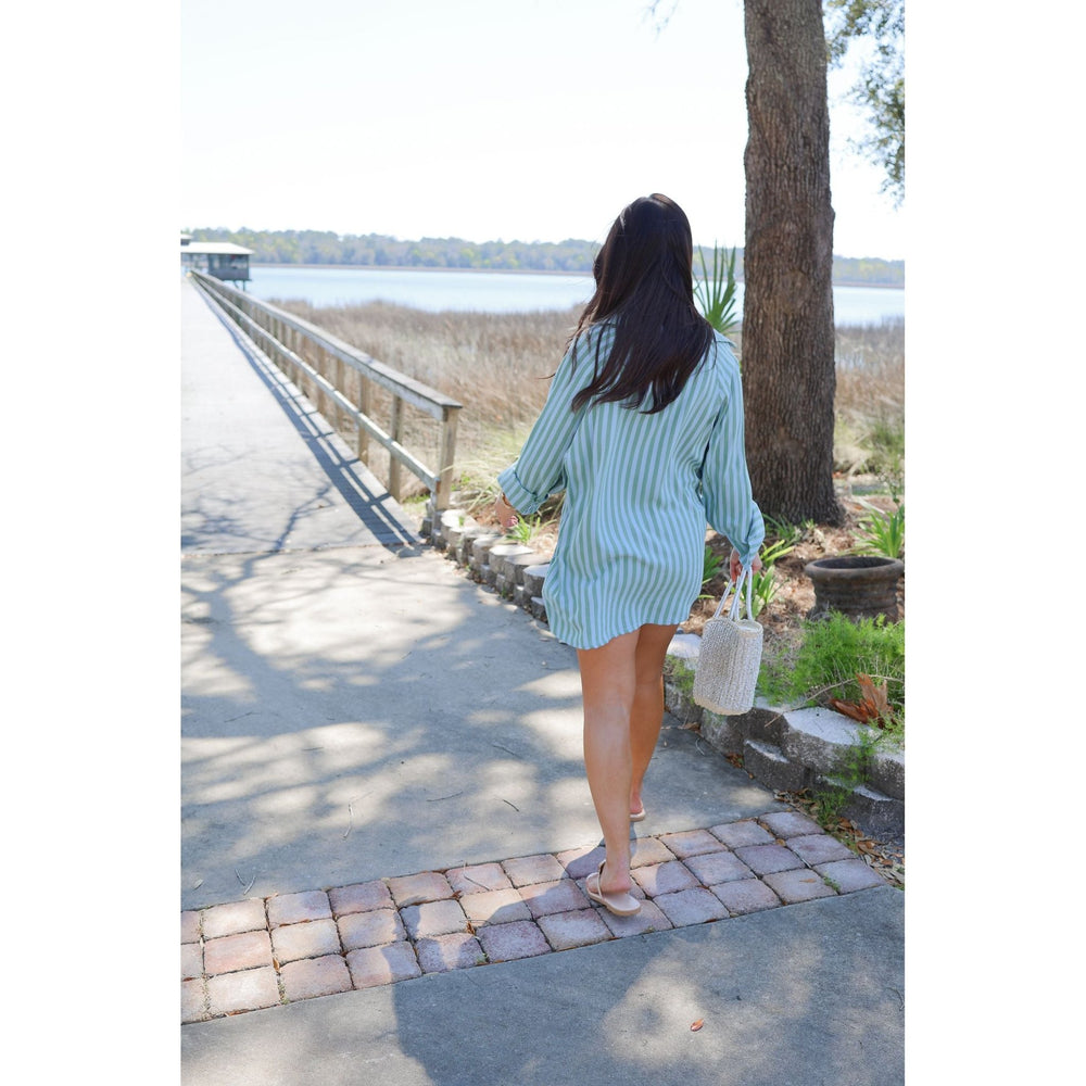 Woman in a light blue shorts set standing on a path by a body of water.