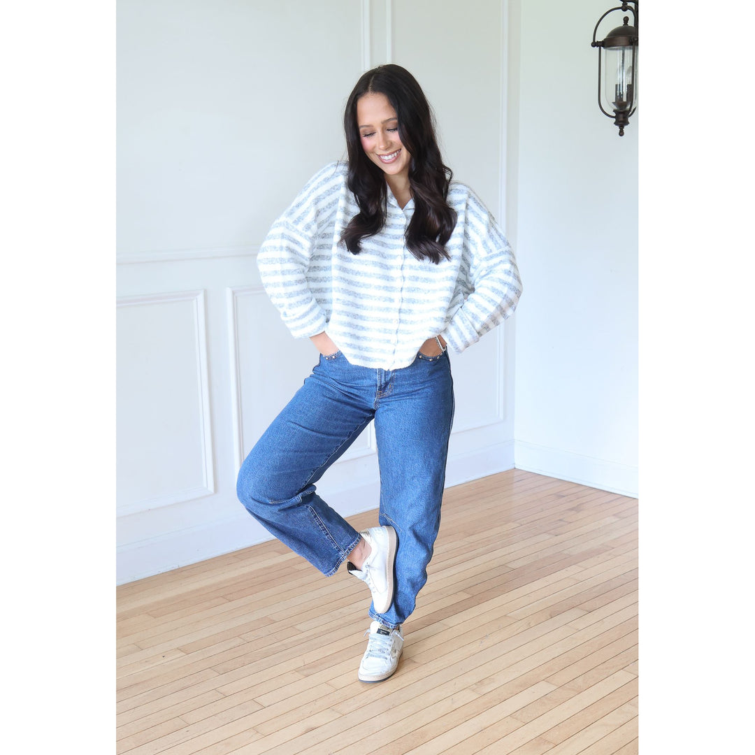 woman wearing gray and white cardigan with blue jeans and sneakers
