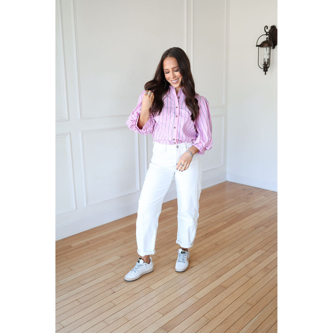 Woman wearing a pink checkered shirt and white pants in a room with wooden flooring and white walls.