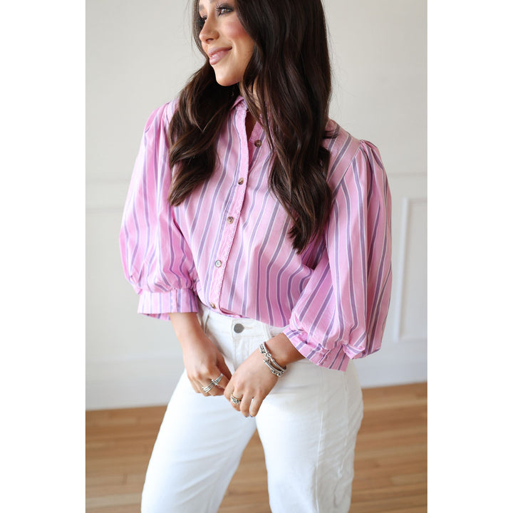 Woman wearing a pink striped blouse and white pants indoors.