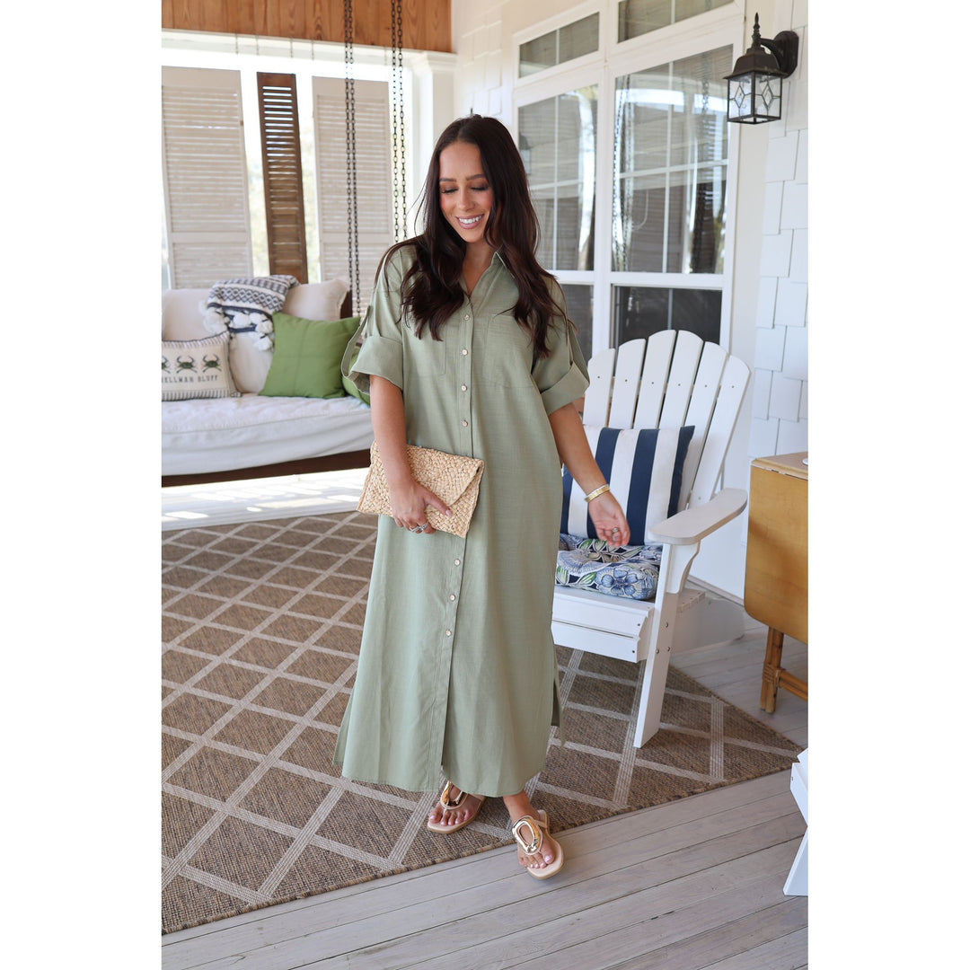 Woman in a green dress standing on a wooden deck with a white chair and rug in the background.