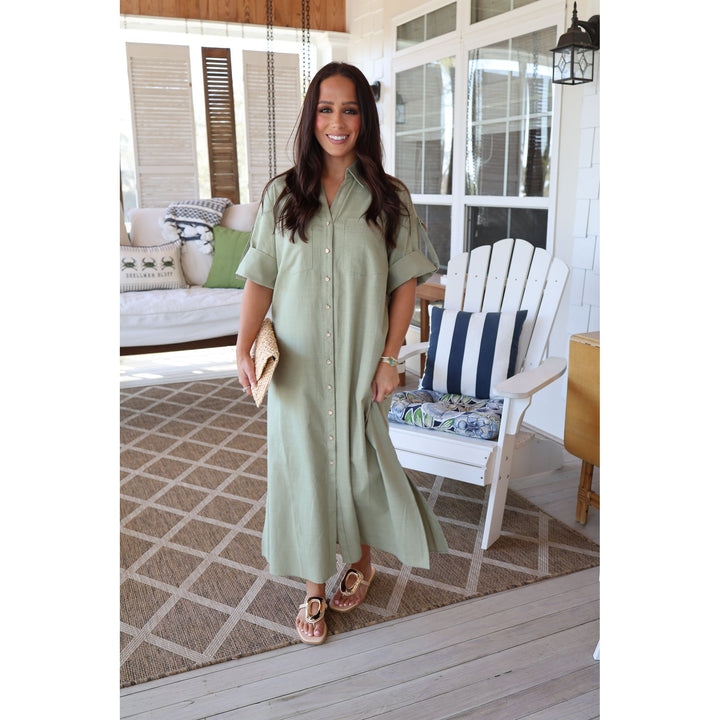 Woman in a light green dress standing on a porch with a white chair and couch in the background.
