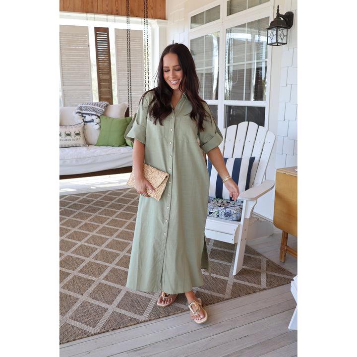 Woman in a green dress standing on a porch with a white chair and table in the background.