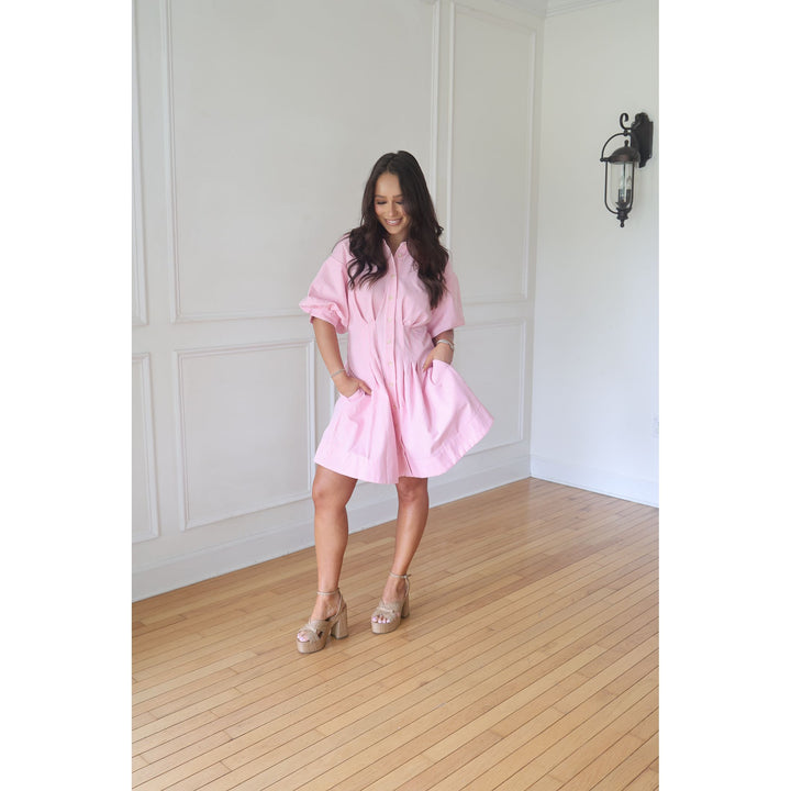 Woman in a pink dress standing in a room with wooden flooring and white walls.