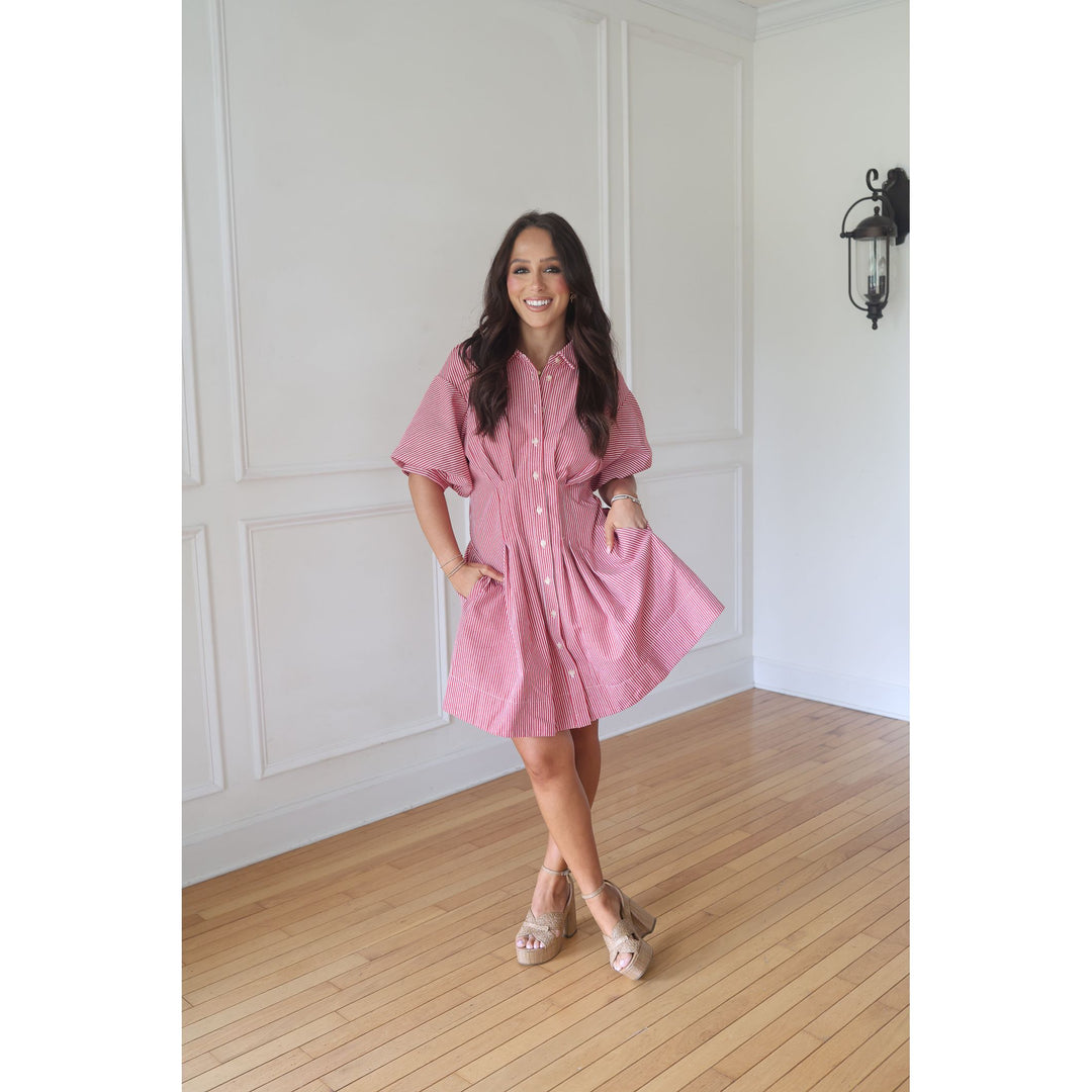 Woman wearing a pink dress standing in a room with wooden flooring and white walls.