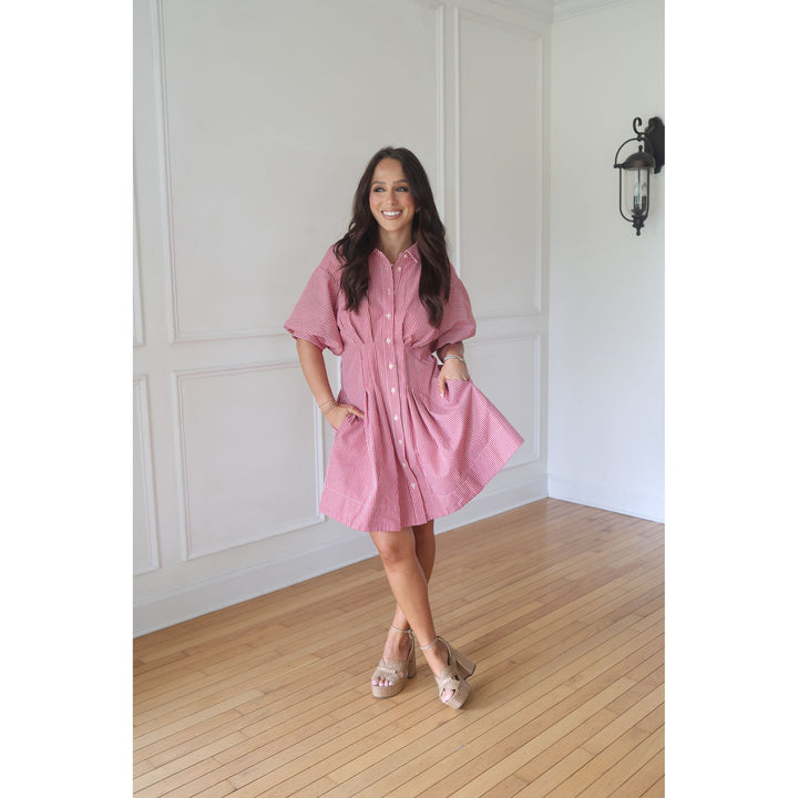 Woman wearing a pink dress standing in a room with white walls and wooden flooring.