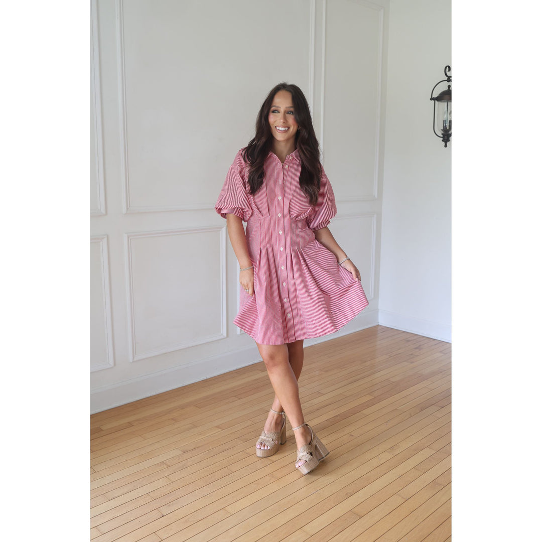 Woman wearing a pink dress standing in a room with wooden flooring and white walls.