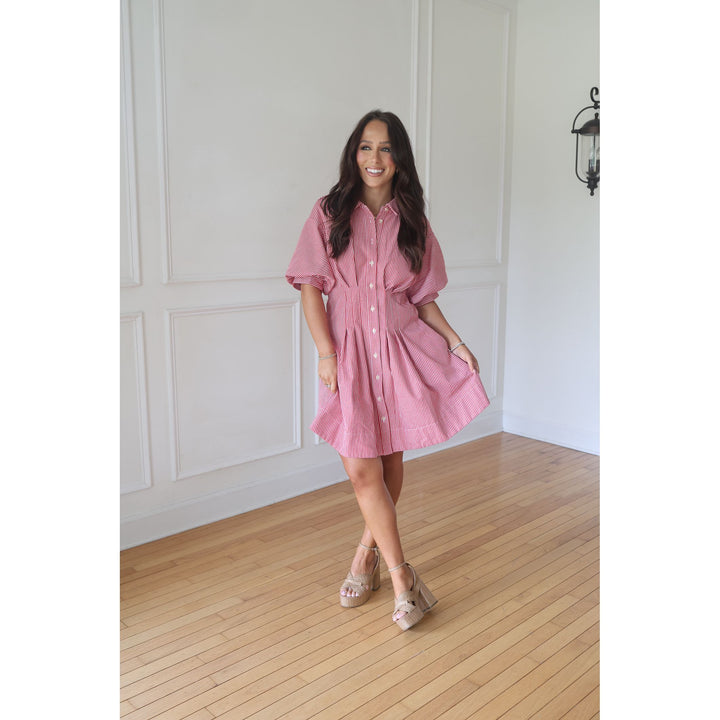 Woman wearing a pink dress standing in a room with wooden flooring and white walls.