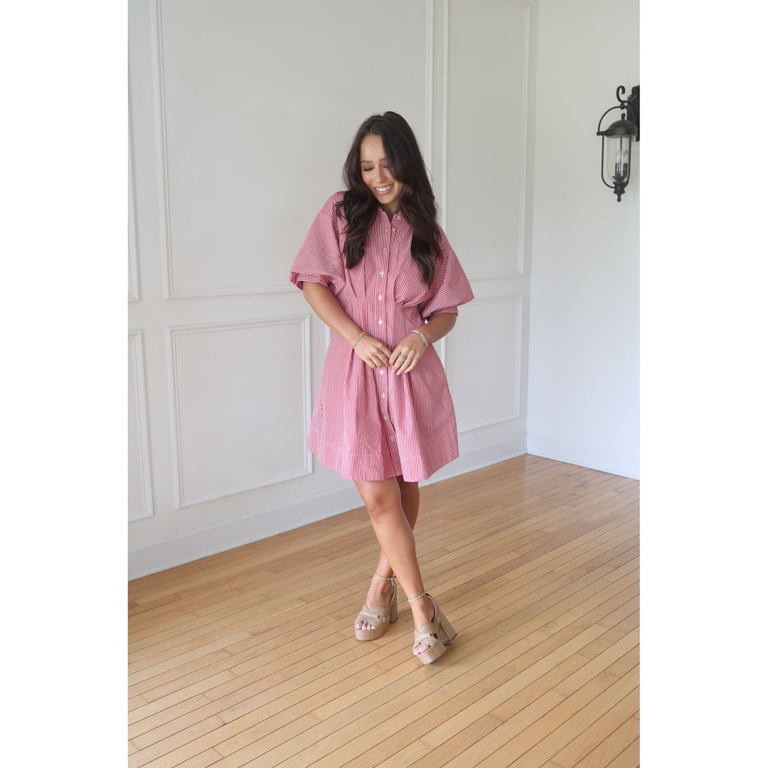 Woman wearing a pink dress standing in a room with wooden flooring and white walls.