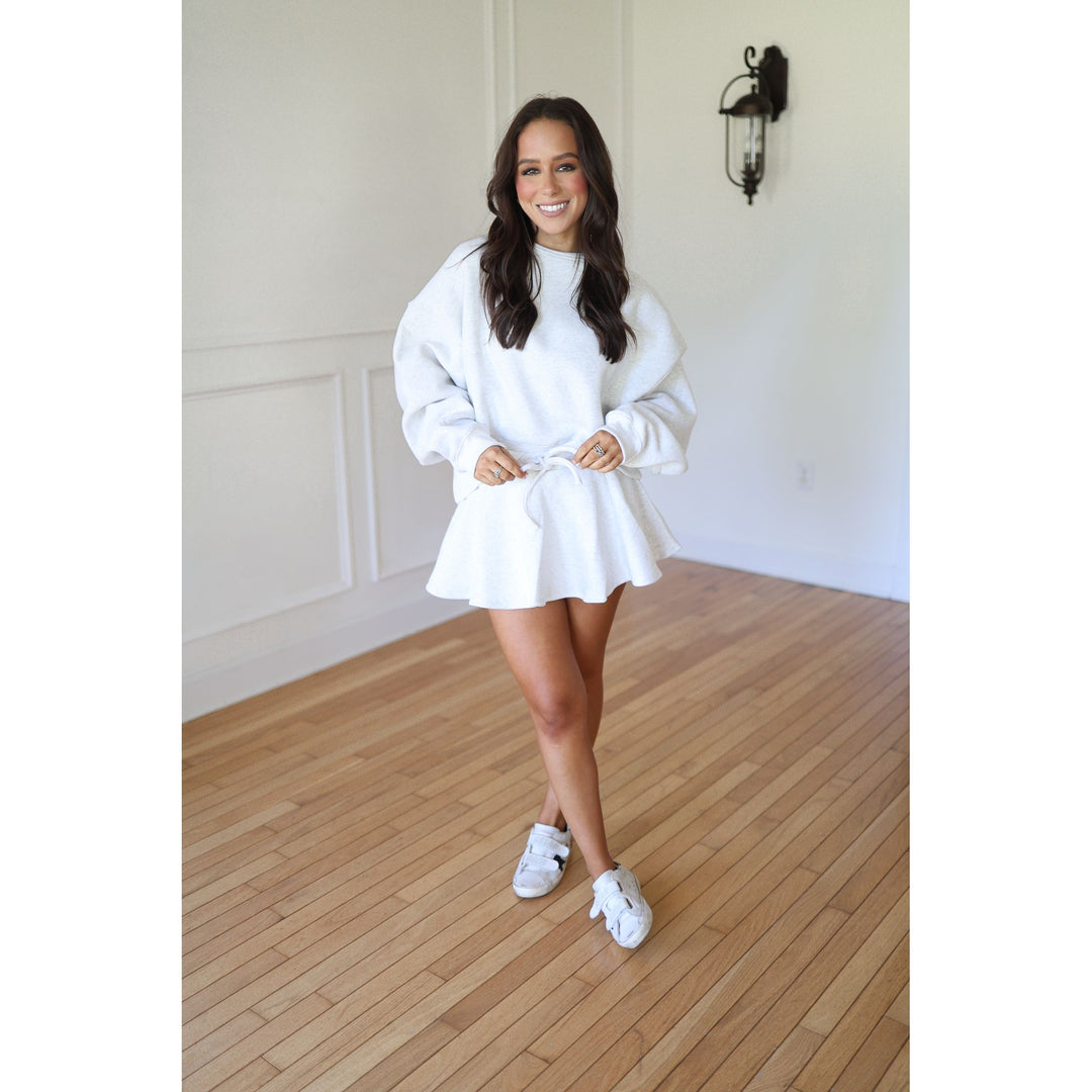 Woman wearing a gray oversized sweater and skirt with white sneakers