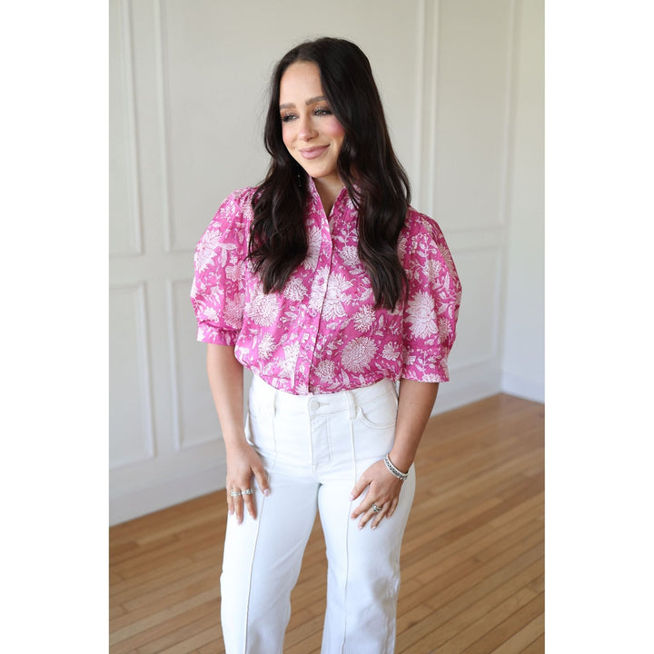 Woman wearing a pink floral blouse and white pants indoors.