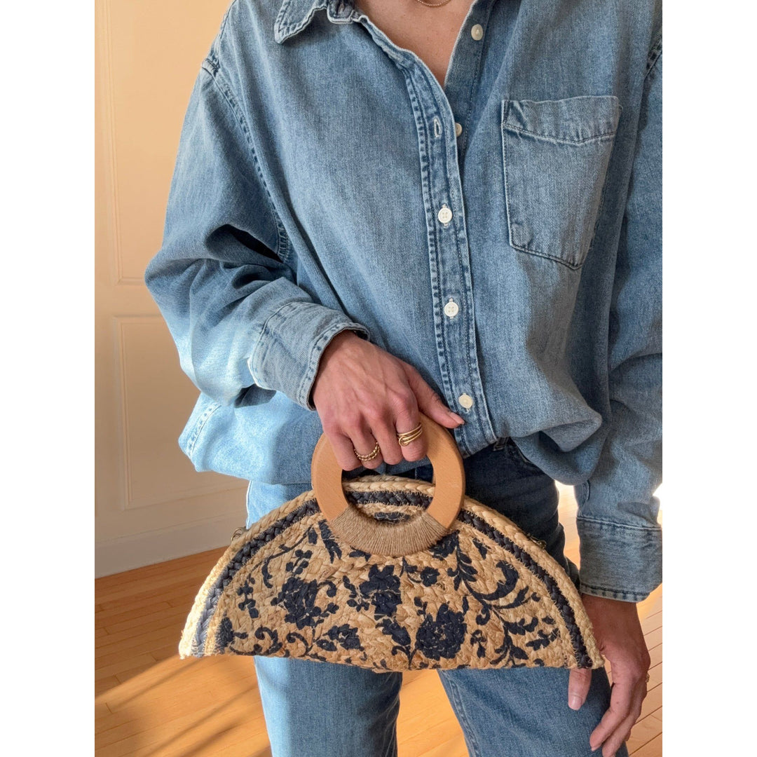 Person holding a floral-patterned handbag with wooden handle against a neutral background