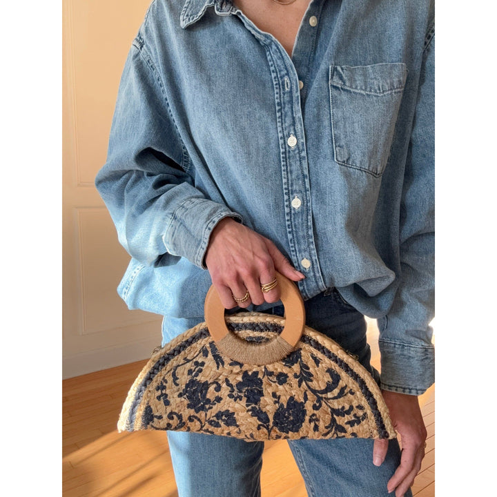 Person holding a floral-patterned handbag with wooden handle against a neutral background