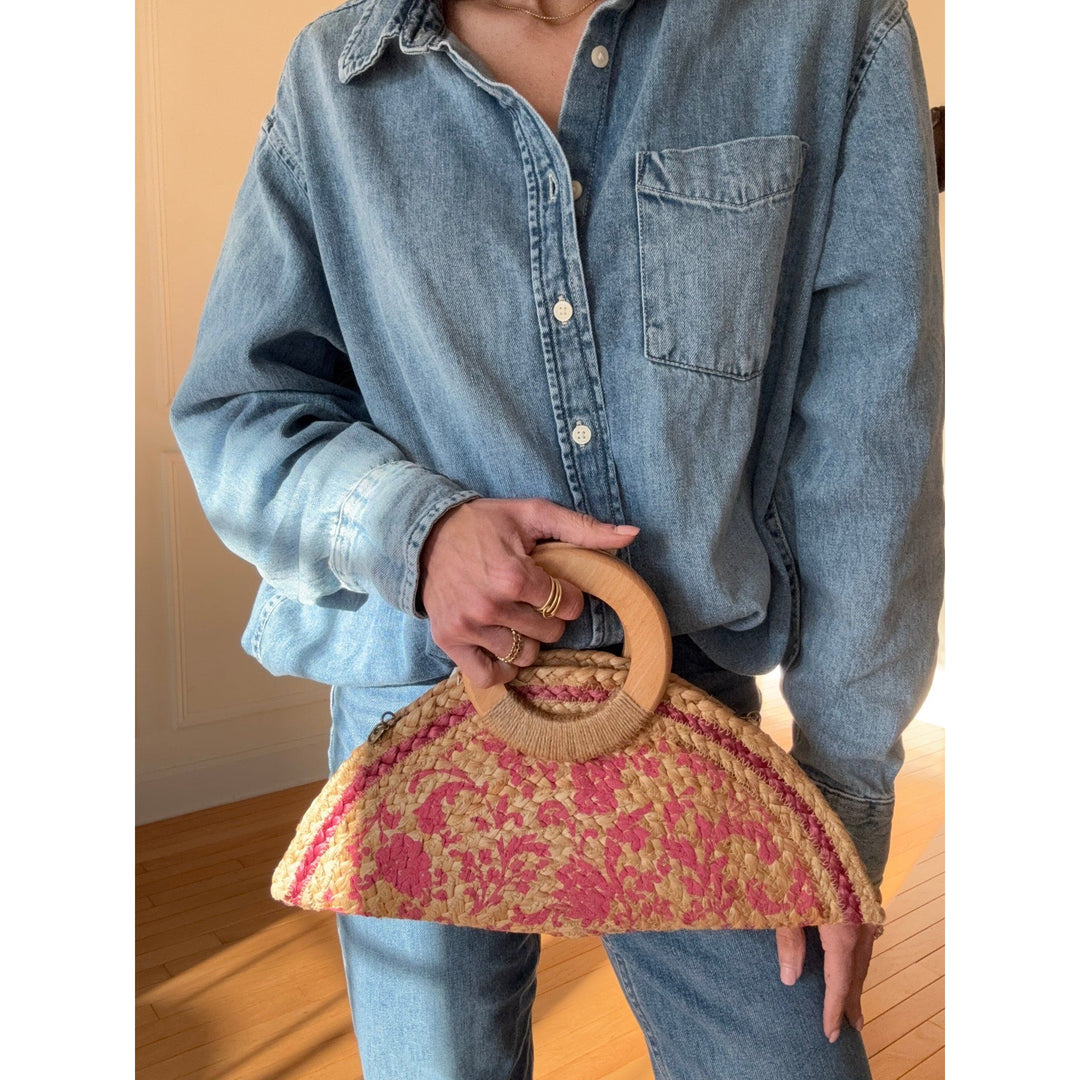 Person holding a decorative handbag with a wooden handle against a neutral background