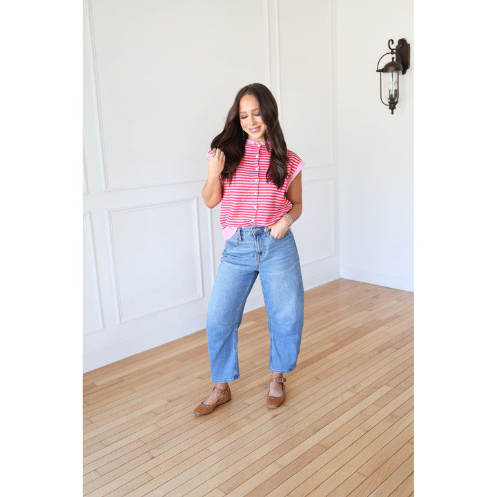 Woman wearing a pink striped shirt and blue jeans standing on a wooden floor.