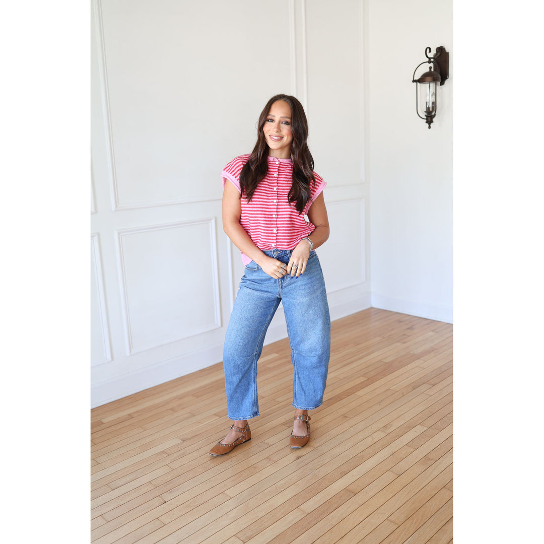 Woman wearing a striped shirt and blue jeans standing in a room with wooden flooring and white walls.