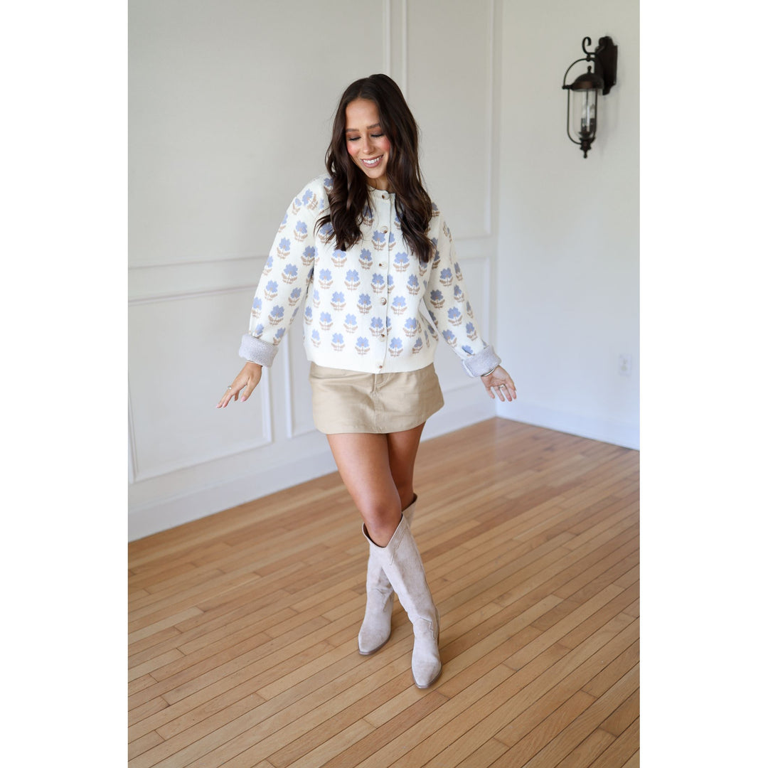Woman wearing a patterned shirt and beige shorts with white knee-high boots 