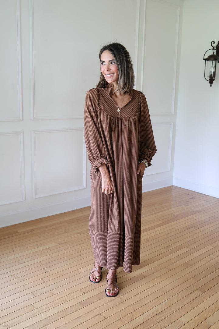 A woman wearing a brown ribbed maxi dress with a V-neckline and long sleeves