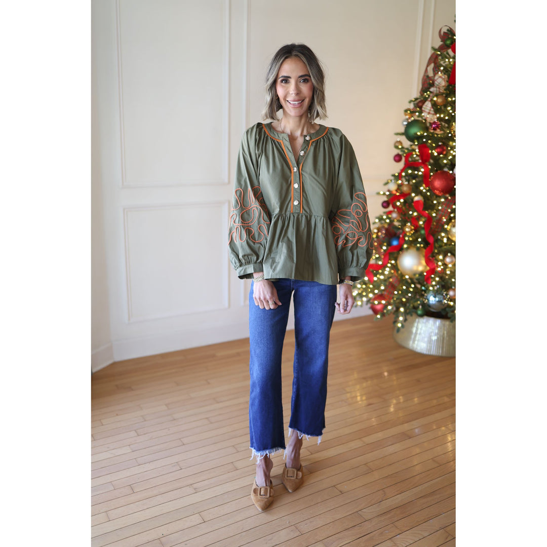 Woman wearing a green blouse with embroidery in front of a decorated Christmas tree.