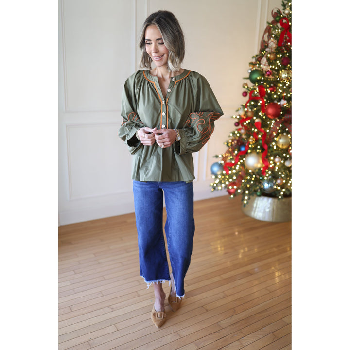 Woman in green top and blue jeans standing in a room with a decorated Christmas tree.