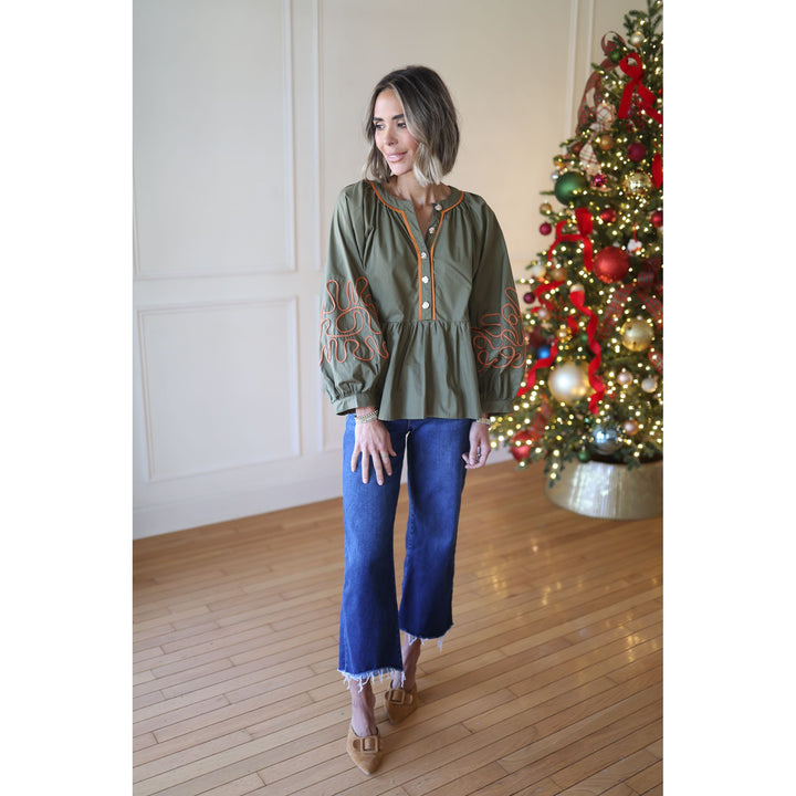 Woman wearing a green blouse with embroidery in front of a decorated Christmas tree.