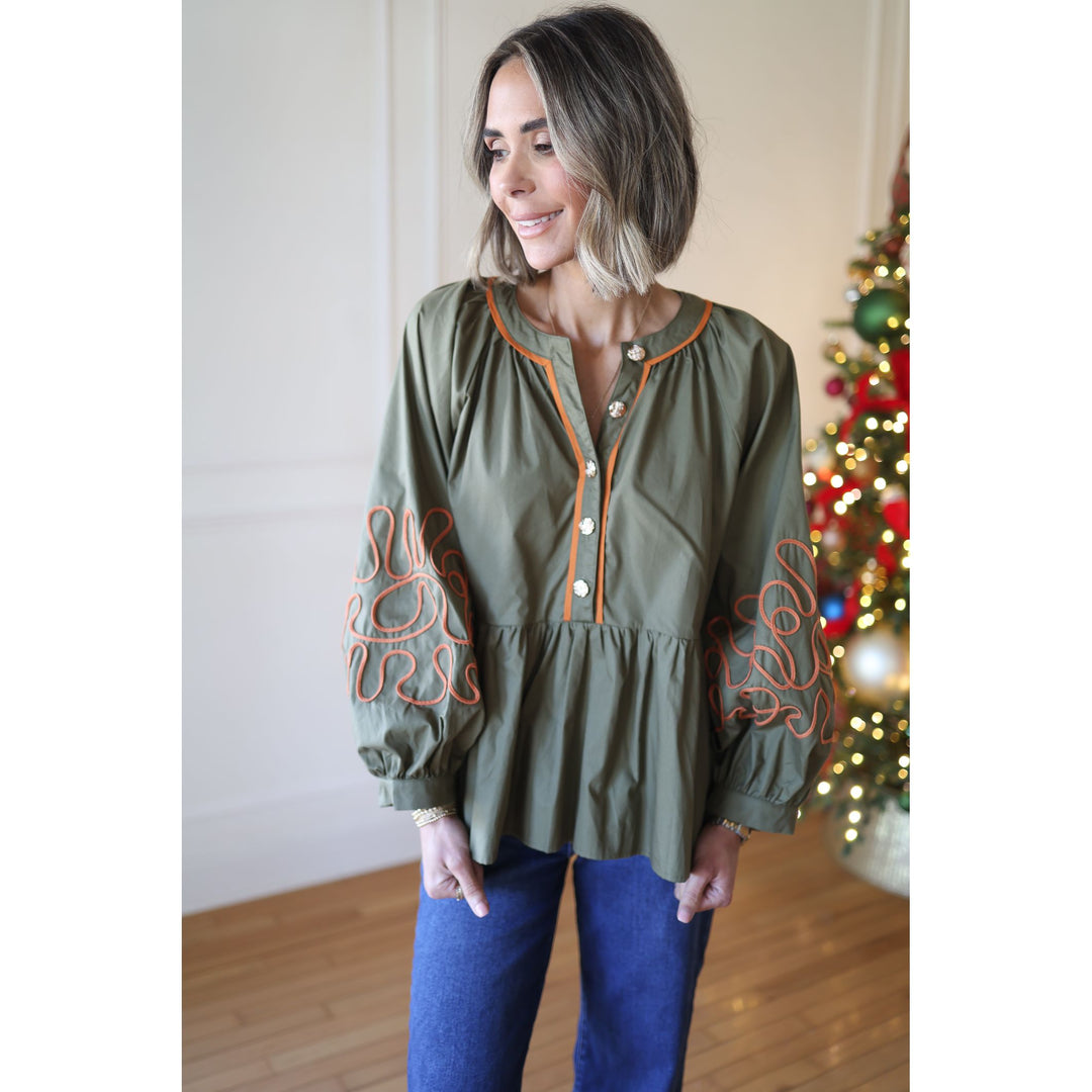 Woman wearing an olive green blouse with orange embroidery in front of a decorated Christmas tree.