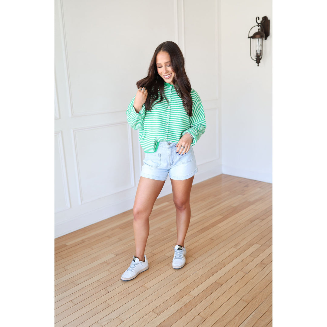 Woman in a green striped shirt and white shorts standing on a wooden floor.