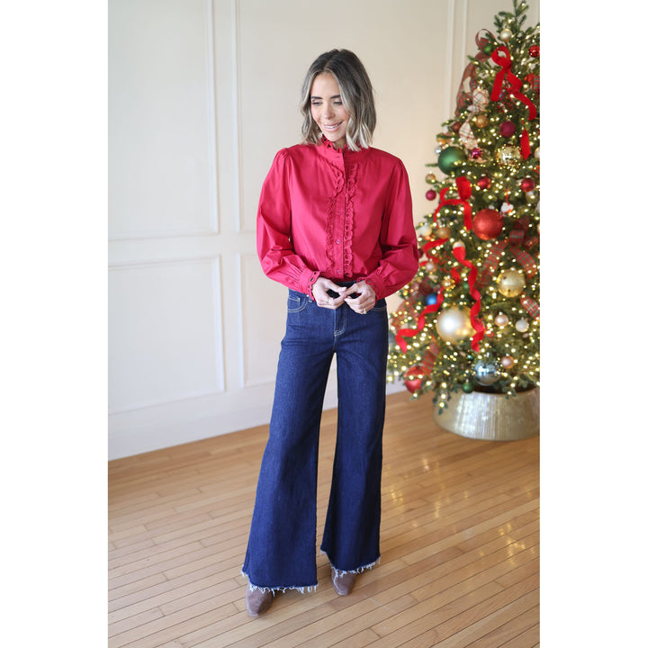 Woman in a wine blouse and blue jeans standing in front of a decorated Christmas tree.