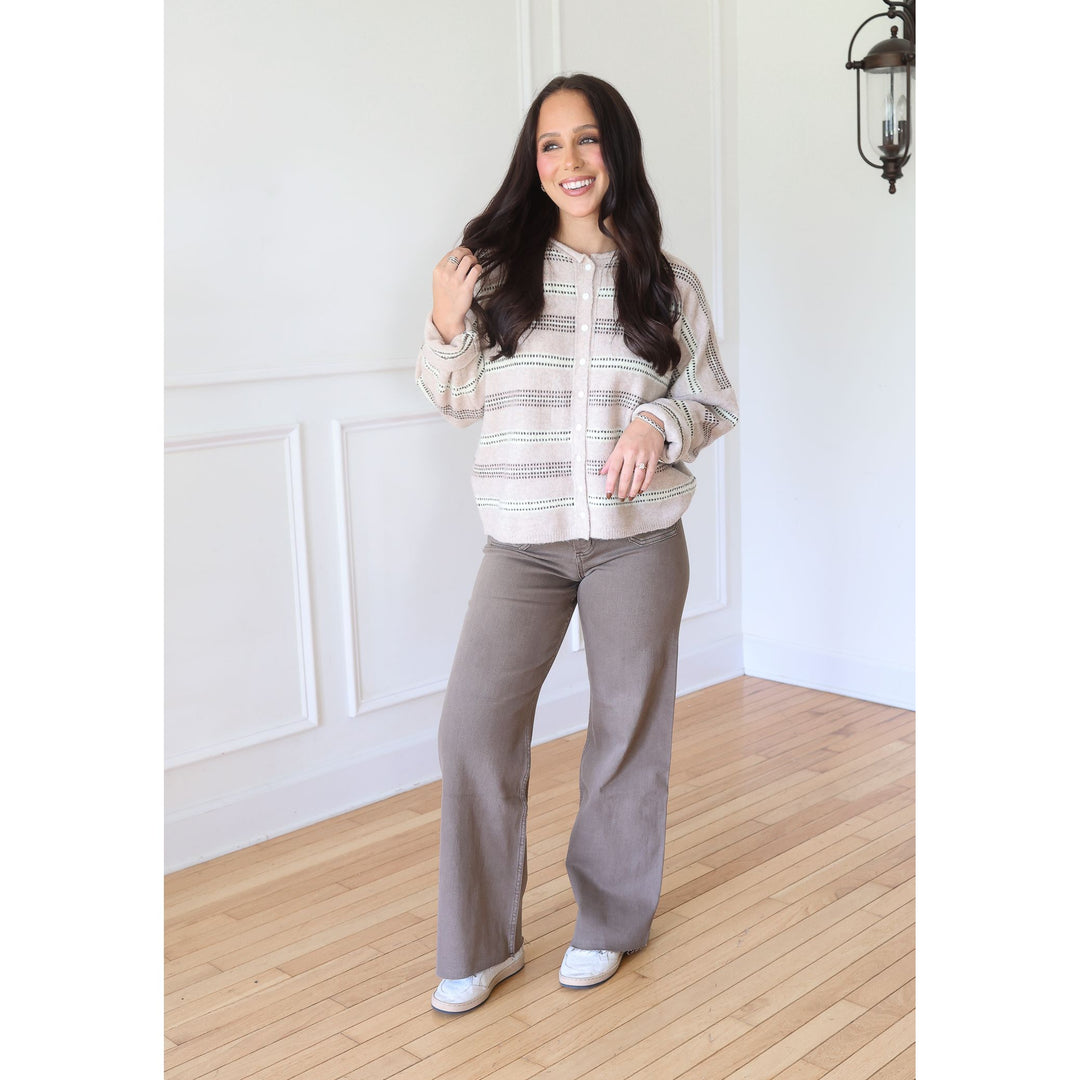 A woman stands wearing a cream and taupe striped zip-up cardigan, taupe wide-leg pants, and white sneakers.