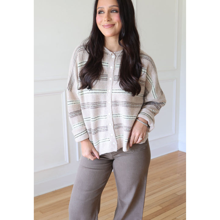 A woman wearing a beige knit cardigan with thin green and gray striped patterns, paired with taupe pants