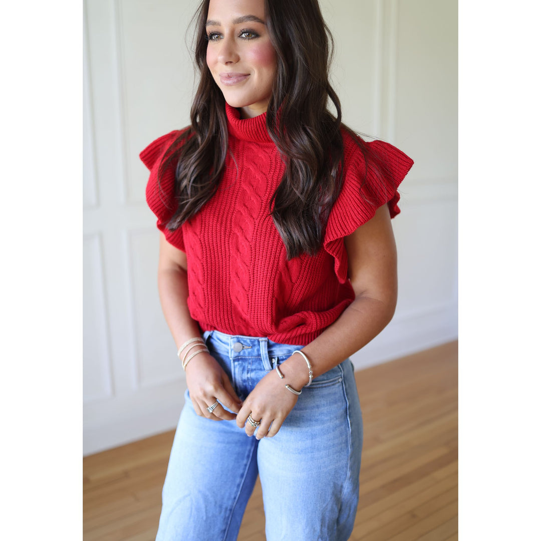 Woman wearing a red ruffled sweater and blue jeans indoors.